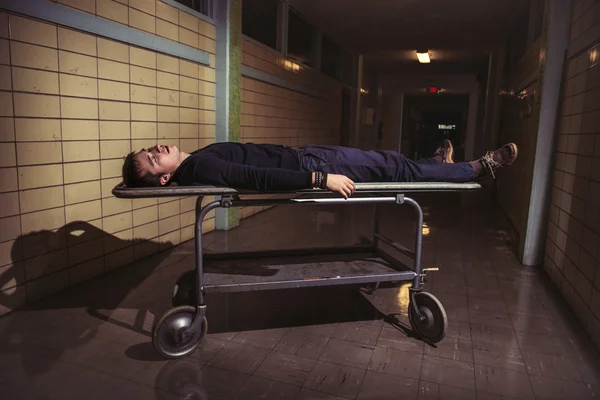 Чоловік лежить на медичному ноші пацієнта в старій лікарні жахів — стокове фото