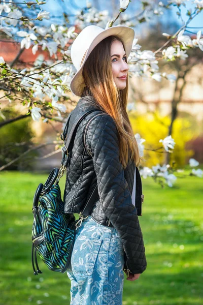 Beautiful fashion hipster woman in spring city garden wearing leather coat and bag