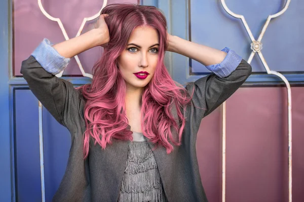 Modelo de moda hipster bonita com cabelo rosa encaracolado posando na frente da parede colorida — Fotografia de Stock