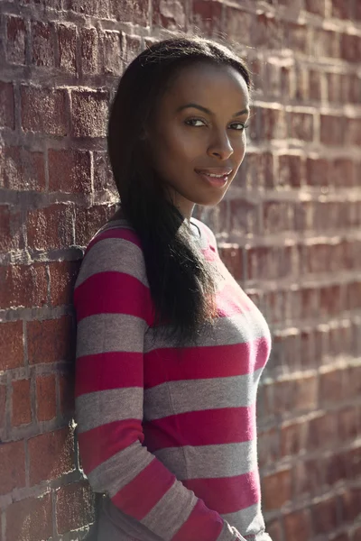 Hermosa afroamericana estudiante mujer vistiendo ropa casual y de pie cerca de la pared de ladrillo al aire libre — Foto de Stock