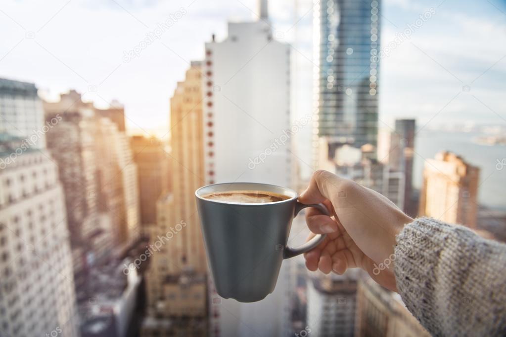 Man holding coffee cup in luxury penthouse apartments with view to New York City Manhattan downtown