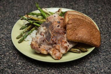 Artış, kahverengi ekmek, domuz biftek ve kuşkonmaz masada yeşil plaka üzerinde servis