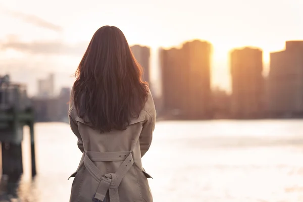 Beautiful lonely girl waiting for somebody near the water at sunset time — Stock Photo, Image