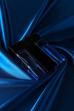 Mavi ipek katlanmış kumaş kaplı parfüm şişesinde parfüm şişesi koyu boş arka planda. Üst görünüm. 