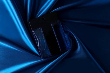 Mavi ipek katlanmış kumaş kaplı parfüm şişesinde parfüm şişesi koyu boş arka planda. Üst görünüm. 