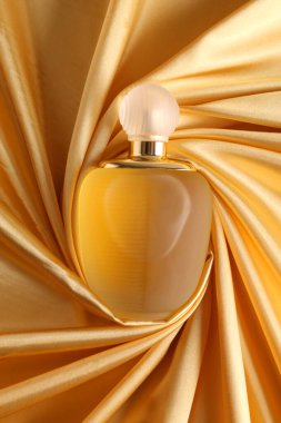 Altın sarısı ipek üzerinde parfüm şişesi katlanmış kumaş arka plan parfüm şişesi koyu boş arka planda. Üst görünüm. 