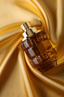 Altın sarısı ipek üzerinde parfüm şişesi katlanmış kumaş arka plan parfüm şişesi koyu boş arka planda. Üst görünüm. 
