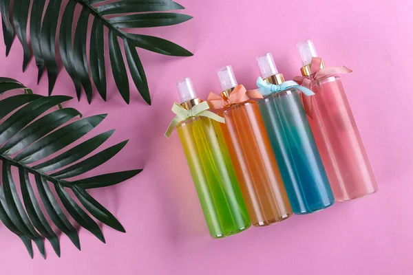 Plastik yüz nemlendirici, saç spreyi veya vücut sisi ve pastel pembe arka planda izole edilmiş yeşil bitkisel yapraklar, deri döşeme, üst manzara, fotokopi alanı, doğal organik güzellik ürünü.