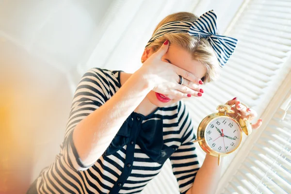 Young pinup woman showing alarm clock and hiding face — Stock Photo, Image