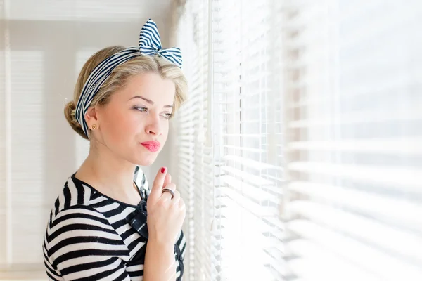 Schöne blonde Pinup-Frau blickt nachdenklich durch Jalousie-Fenster — Stockfoto