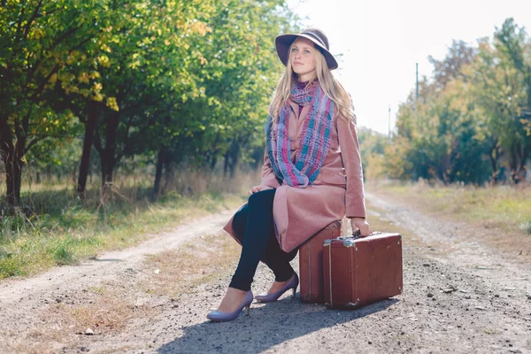 Klasik valizli yalnız bir kadın boş yolda otostop çekiyor. — Stok fotoğraf