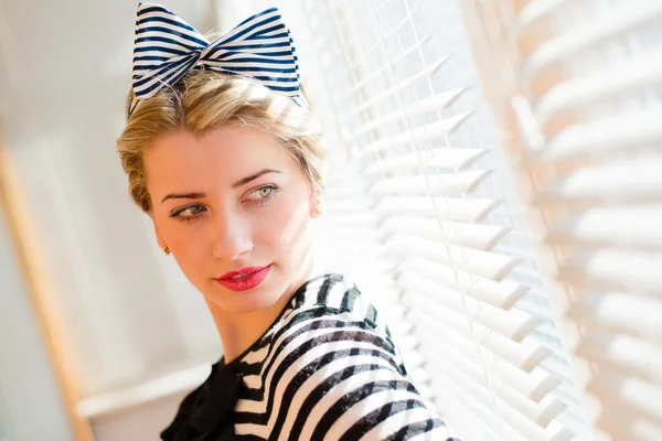 Beautiful blond pinup woman looking thoughtfully through jalousie windows — Stock Photo, Image