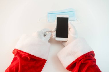 Tıbbi maskeli akıllı telefonlu Noel Baba. İnternetten selamlar, Noel ve yeni yıl için servis siparişleri. Koronavirüs salgınında sosyal uzaklık, yeni bir gerçeklik. Boşluğu kopyala