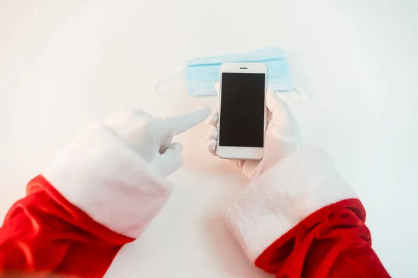 スマートフォンを備えた医療用マスクのサンタクロース オンライン挨拶 クリスマスと新年のためのサービスを注文する コロナウイルスの流行の社会的距離 新しい現実 スペースのコピー — ストック写真