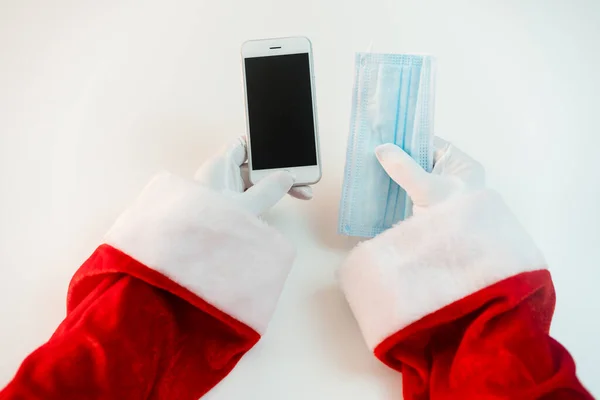 スマートフォンを備えた医療用マスクのサンタクロース オンライン挨拶 クリスマスと新年のためのサービスを注文する コロナウイルスの流行の社会的距離 新しい現実 スペースのコピー — ストック写真