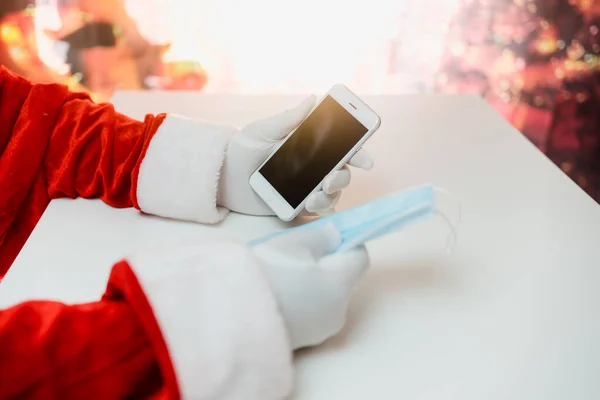 スマートフォンを備えた医療用マスクのサンタクロース オンライン挨拶 クリスマスと新年のためのサービスを注文する コロナウイルスの流行 新しい現実の社会的距離 — ストック写真