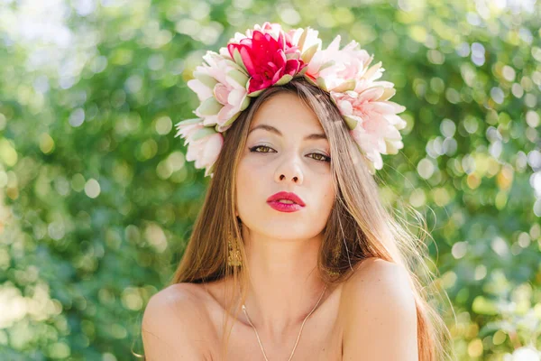 美しいブルネットの若い女性の肖像画で蓮の花冠とピンクの口紅のメイクポージング優美に上の緑の公園Bokeh屋外コピースペース背景 ロイヤリティフリーのストック画像
