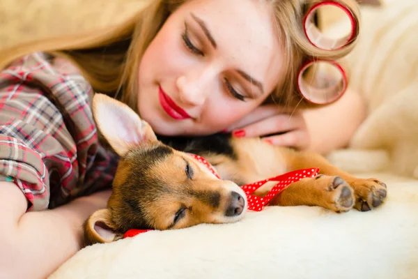 Sleeping beauties picture: closeup portrait of pinup girl beautiful blond young woman with curlers having fun sleeping or dreaming with her little puppy dog happy smiling on bed — Stock Photo, Image