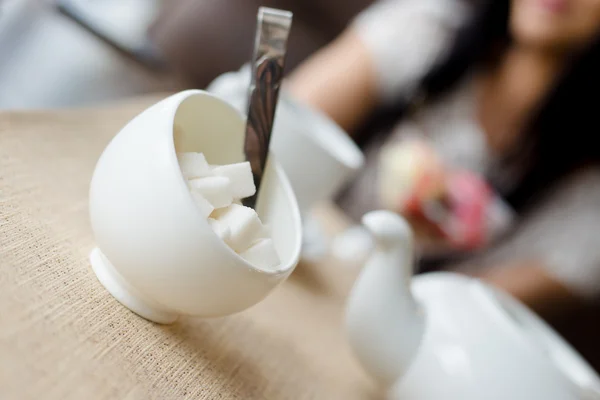 Primo piano su zuccheriere bianche pressate e cucchiaio di metallo con bollitore per tè su sfondo caffetteria o ristorante — Foto Stock