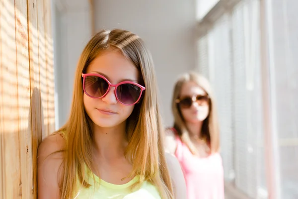 Picture of 2 playful  in sun glasses best girl friends or sisters beautiful blond young women having fun posing happy smiling and looking at camera on sun lighted windows background picture — Stock Photo, Image