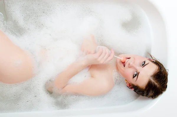 Sweet spa time: picture of licking candy beautiful young sensual woman having fun happy smiling relaxing & enjoying lying in spa bath on foam water background — Stock Photo, Image