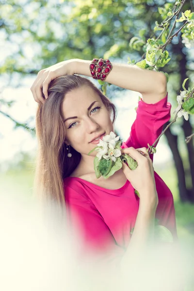 Primer plano retrato de hermosa rubia joven chica bonita con ojos azules de pie bajo el árbol floreciente y mirando a la cámara en la imagen — Foto de Stock