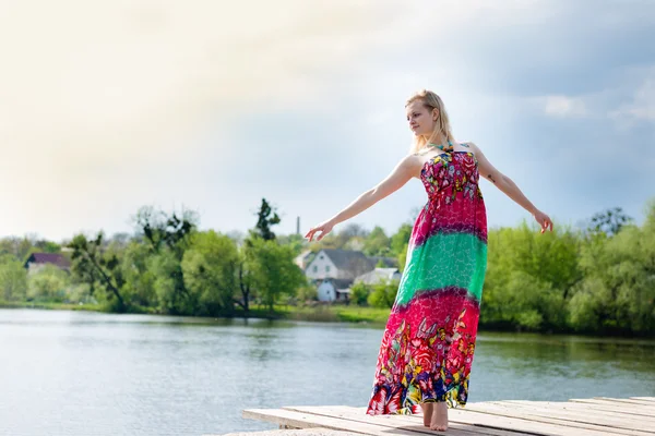 肖像跳舞的女孩美丽的金发碧眼的年轻的女子的苗条伸展长光衣服上水湖绿色的夏天户外 & 蓝色天空背景 — 图库照片