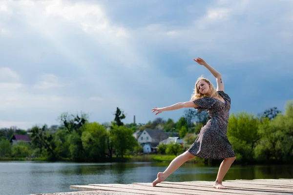 Feeling free: portrait of beautiful blond woman young dancing girl with falling sun lighting rays from blue sky at water lake on spring or summer nature green outdoors background picture — Stock Photo, Image