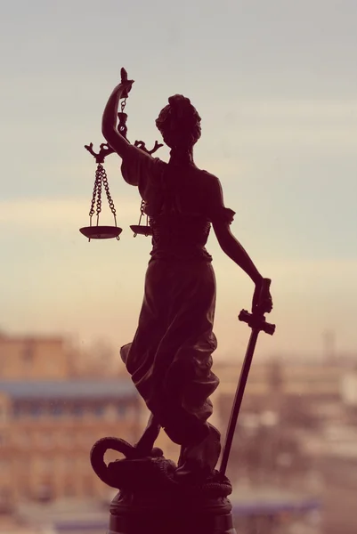 Imagen de la diosa Themis o Lady Justice de pie sobre una ventana sosteniendo la espada con los ojos vendados en el fondo de la ciudad —  Fotos de Stock