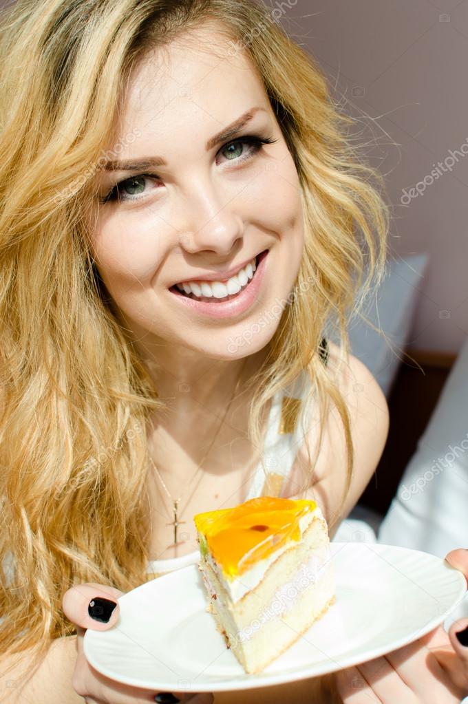 eating alone large fruit creamy cake beautiful blond young woman cute green eyes girl having fun happy smiling & looking at camera on bedroom background closeup portrait picture