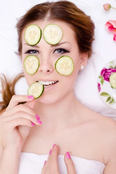 Green natural spa treatment: schöne blonde junge Frau, die Spaß daran hat, Gurkenscheiben auf ihre Gesichtshaut zu kleben, glücklich lächelnd in die Kamera auf weißem Hintergrund blickt — Stockfoto