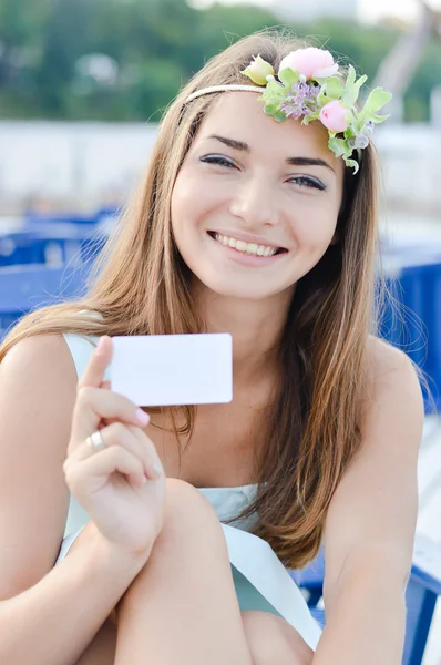 Portrait de belle fille blonde jeune femme ayant plaisir heureux sourire avec des fleurs dans sa tête tenant la carte de visite de l'espace de copie vierge & regardant la caméra sur l'été ou le printemps en plein air image de fond — Photo