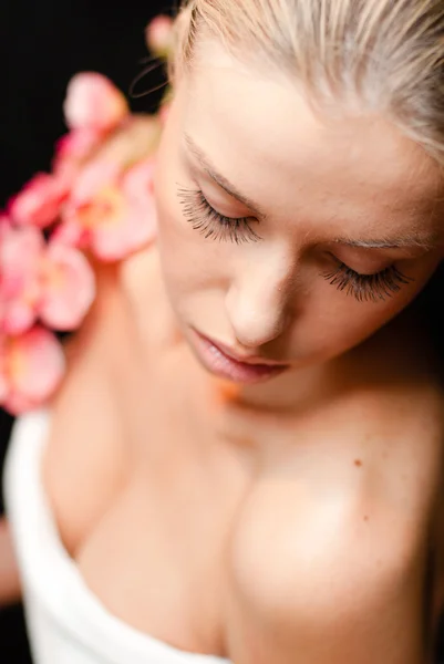 Closeup retrato de menina loira jovem mulher bonita com flor rosa fechando os olhos tendo procedimentos de spa sonhando & isolado em fundo espaço cópia preta — Fotografia de Stock