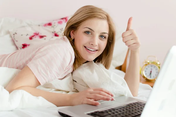 Imagem de mostrar polegar para cima bela doce doce jovem mulher olhos azuis menina loira na cama com laptop pc computador olhando para a câmera em branco cópia espaço fundo close-up retrato — Fotografia de Stock