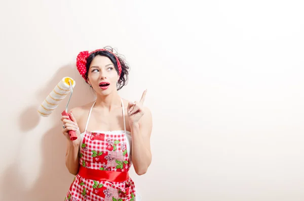 Picture of funny young brunette pinup lady in fun holding paint bolster & having refurbishing idea pointing with finger looking up on white copy space background wall portrait — Stock Photo, Image