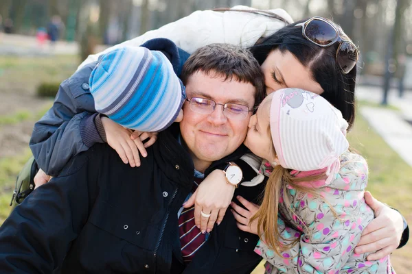 Familia feliz de 4 celebrando primer plano retrato: Padres con dos hijos divirtiéndose abrazando y besando padre que es feliz sonrisa y mirando a la cámara en primavera u otoño día al aire libre fondo —  Fotos de Stock