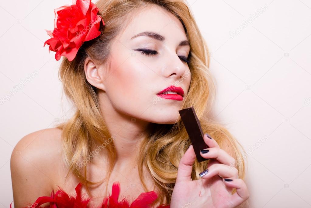 Funny pin up pretty girl attractive blond lady having fun sensually enjoying a bar of chocolate in studio over white or light copy space background closeup portrait picture