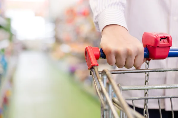 Homem ou mulher na loja com carrinho de compras ou carrinho, close-up na mão sobre o fundo prateleira do supermercado — Fotografia de Stock