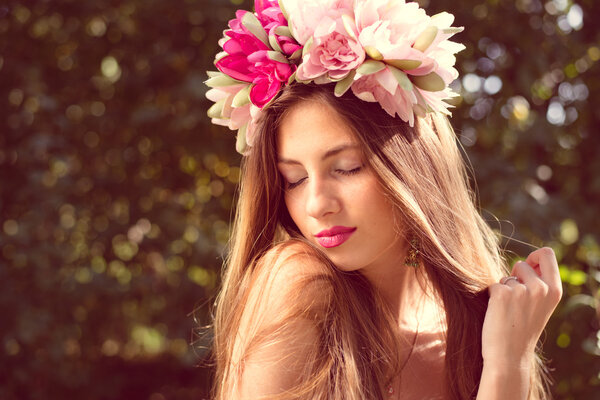 Beautiful fairy: filtered image of brunette pretty girl in lotus flower crown and pink makeup posing gracefully on green outdoors