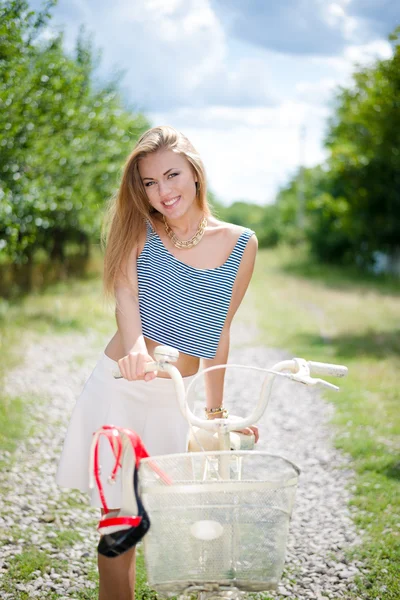 Chica de pie con una bicicleta en la carretera del campo —  Fotos de Stock