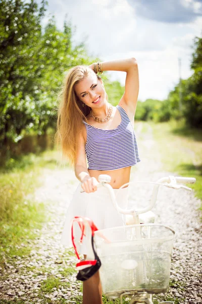 Chica de pie con una bicicleta en la carretera del campo — Foto de Stock