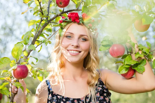 Blond girl smiling among red apples — Stock Photo, Image