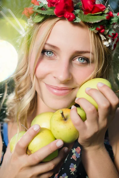 Blond meisje lachend met appels in krans van bloemen — Stockfoto