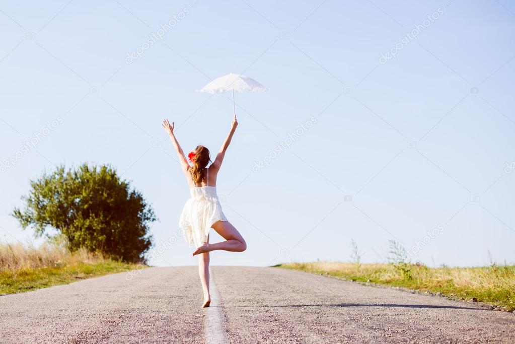 Beautiful ballet dancer with lace white umbrella jumping on highway road over blue sky copy space background