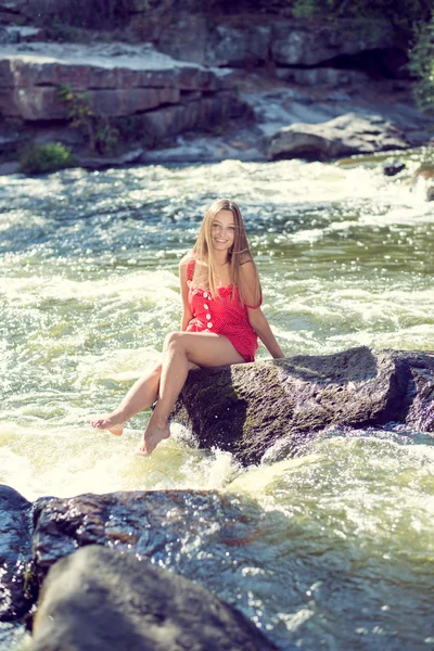 Young woman sitting on rock in fast mountain river and splashing water on summer or early autumn outdoor copy space background — Stock Photo, Image