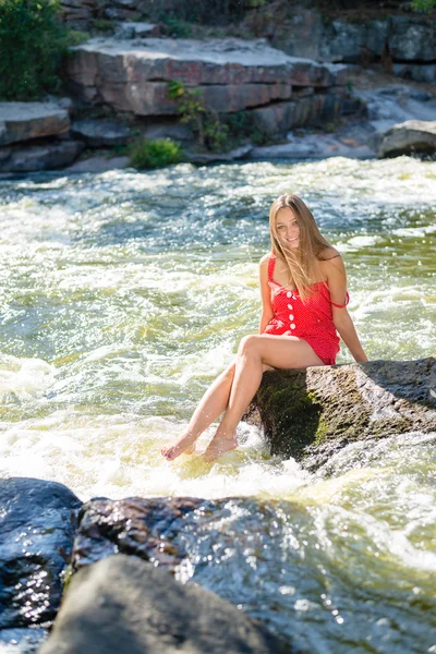Young woman sitting on rock in fast mountain river and splashing water on summer or early autumn outdoor copy space background — Stock Photo, Image