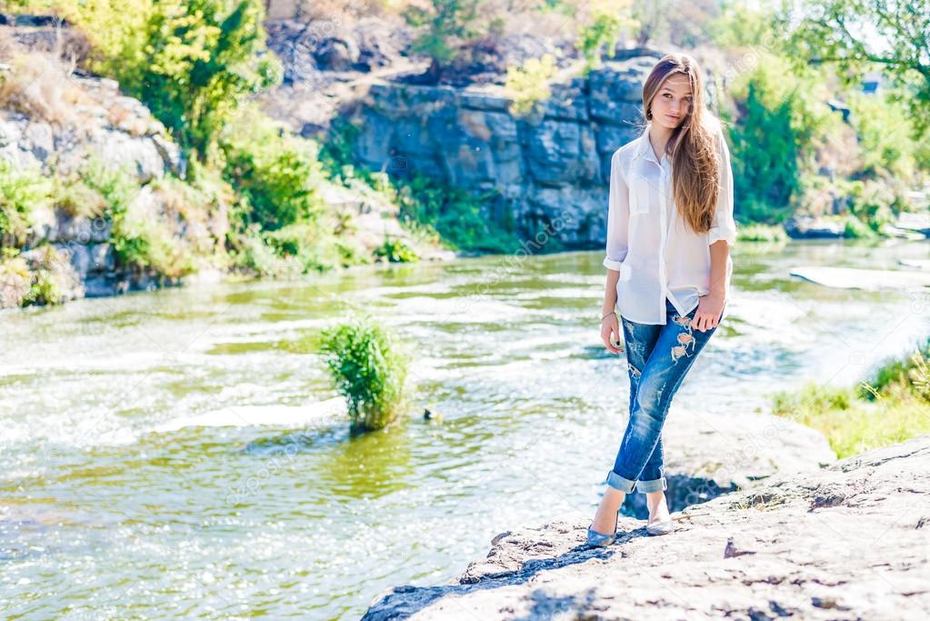 Young woman standing on cliff edge over fast mountain river on summer or early autumn outdoor copy space background