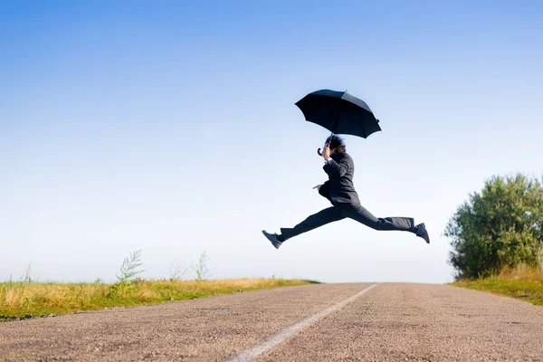 Affärsman med paraply hoppning — Stockfoto