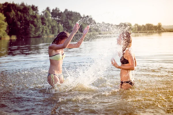 Diversión de verano: imagen filtrada de 2 hermosas mujeres jóvenes o adolescentes mejores amigos divirtiéndose y salpicando agua en el río o el lago al atardecer en el sol al aire libre copiar el espacio de fondo —  Fotos de Stock