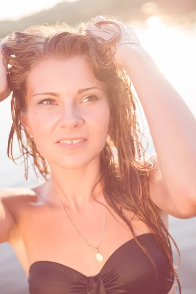 Hermosa mujer sexy en traje de baño con el pelo mojado posando en el cuerpo de agua en el fondo del atardecer de verano —  Fotos de Stock